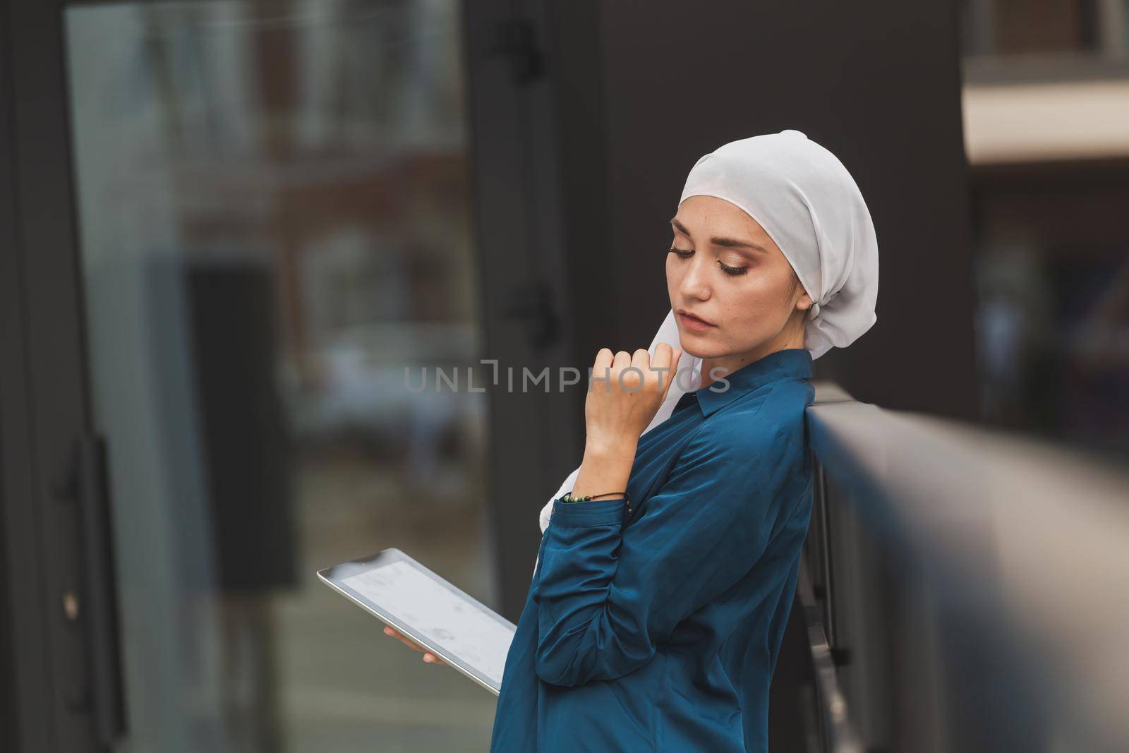 Smiling muslim girl using digital tablet, browsing Internet or social networks outdoor.
