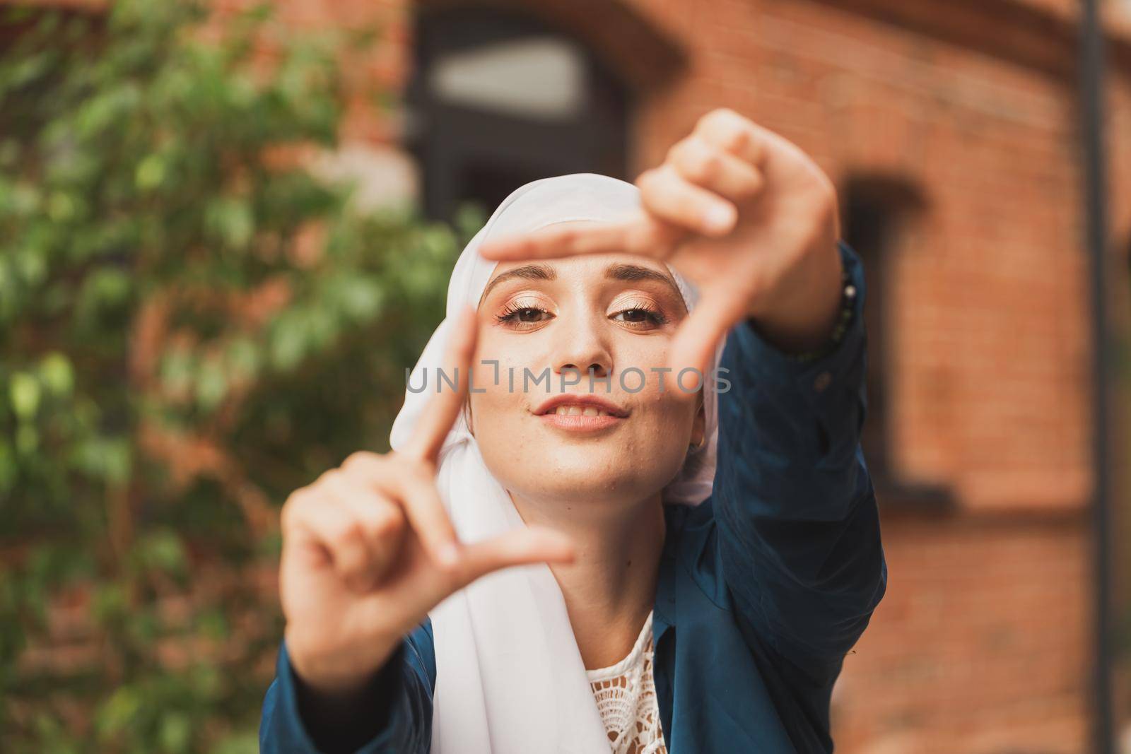 Portrait of young muslim girl making a camera frame with fingers outdoors. by Satura86