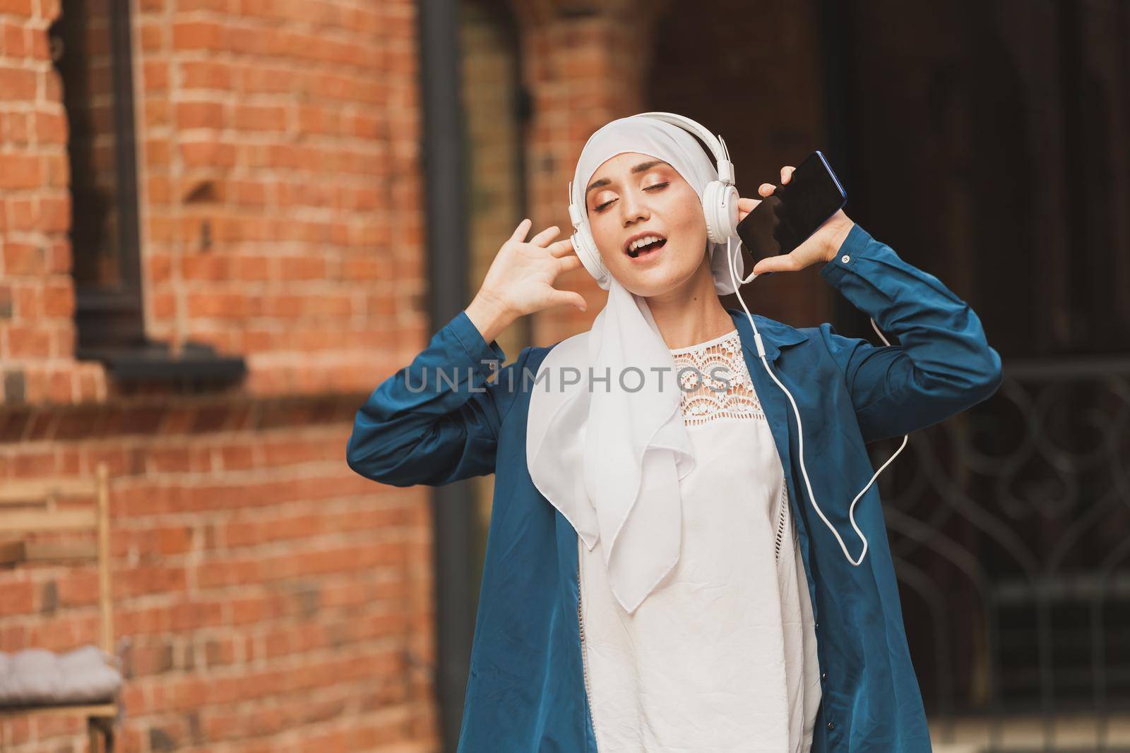 Portrait of young arabian muslim woman listening music with headphone and dancing. Feminism, woman independence and leisure concept