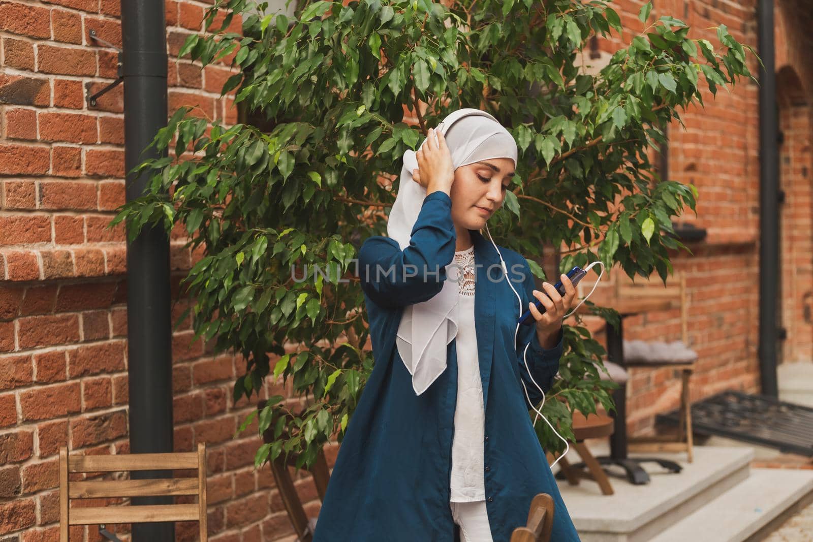 Portrait of young modern arabian woman holding mobile phone and listening the music to headphone