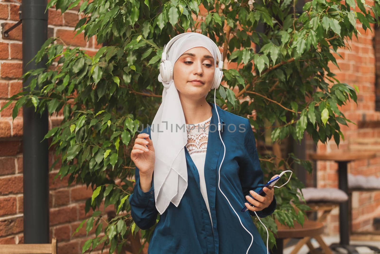 Portrait of young modern arabian woman holding mobile phone and listening the music to headphone