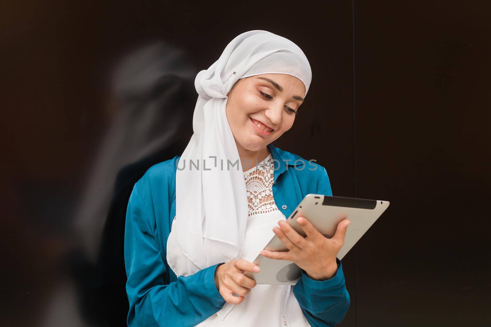 Smiling muslim girl using digital tablet, browsing Internet or social networks outdoor.