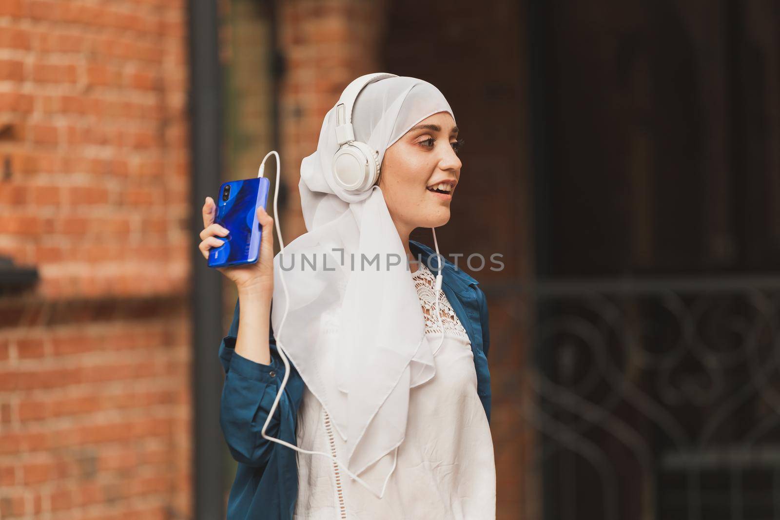 Portrait of young modern arabian woman holding mobile phone and listening the music to headphone