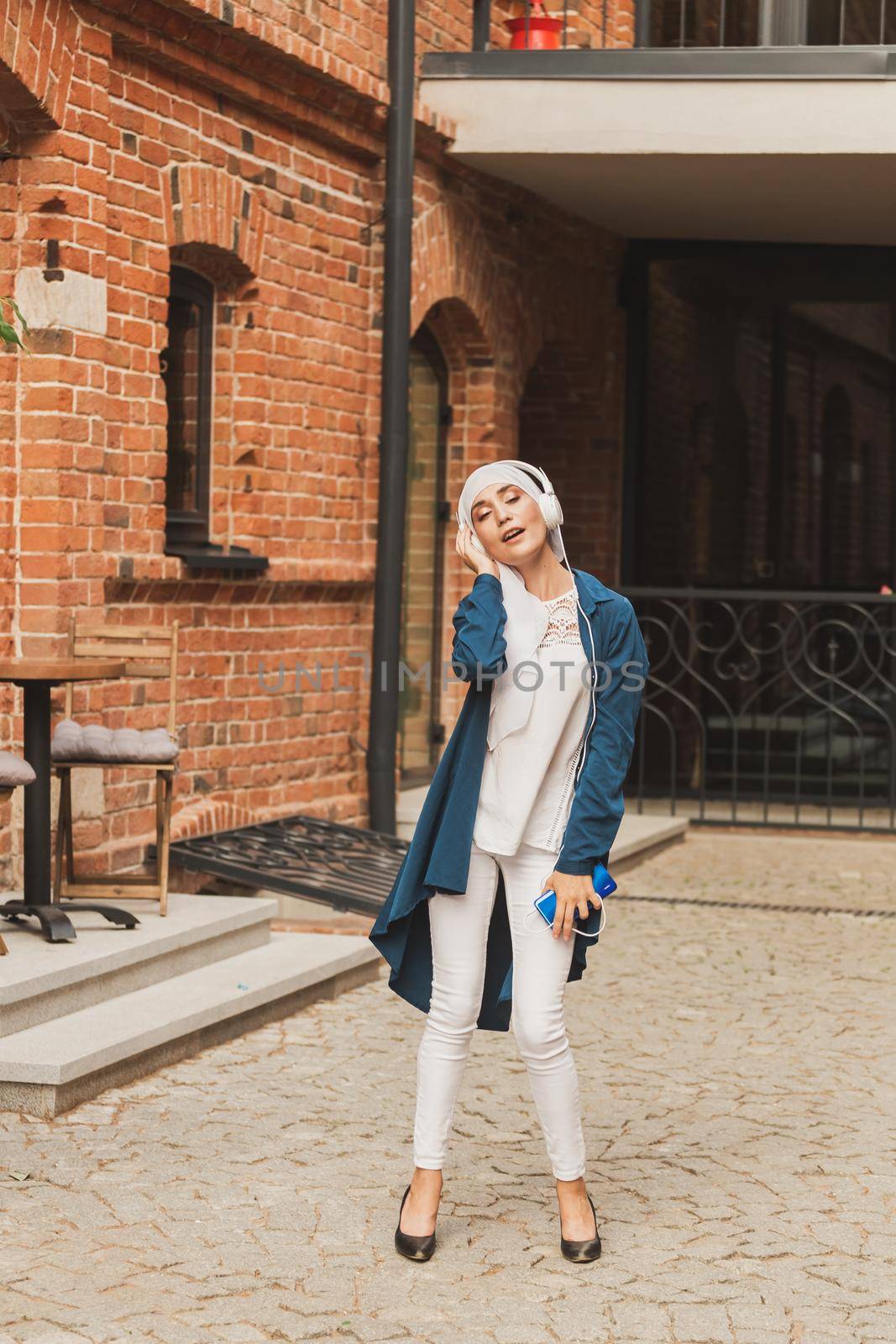 Portrait of young arabian muslim woman listening music with headphone and dancing. Feminism, woman independence and leisure concept. by Satura86