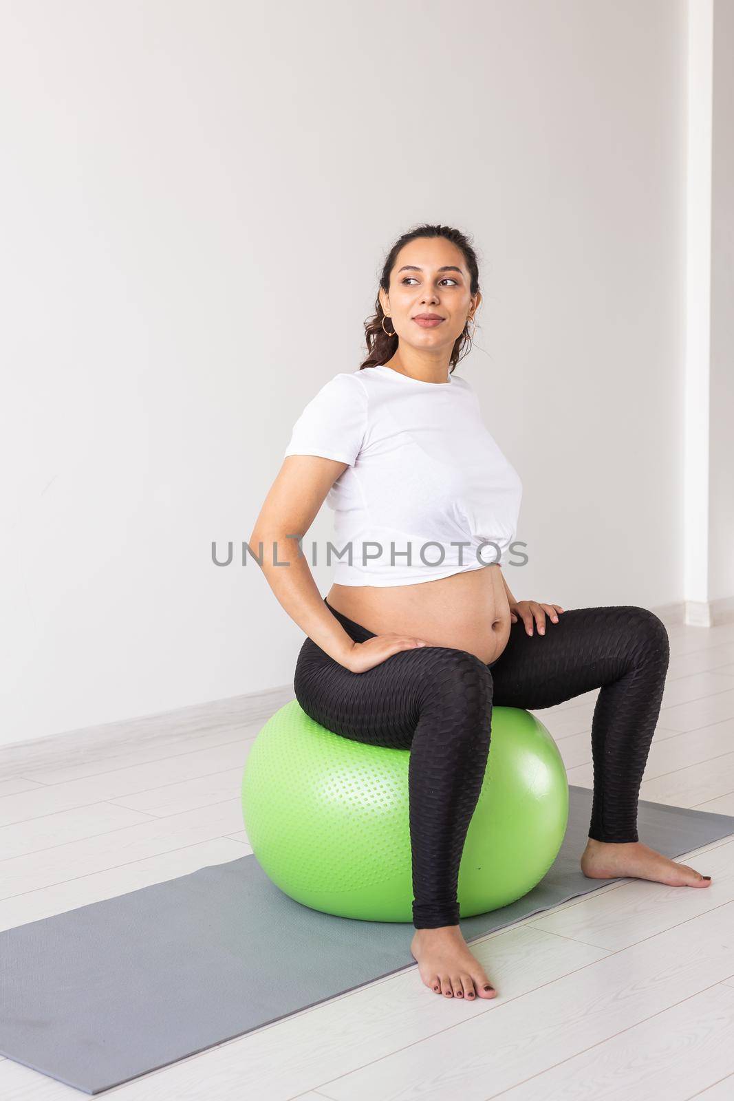 A young pregnant woman doing relaxation exercise using a fitness ball while sitting on a mat. by Satura86