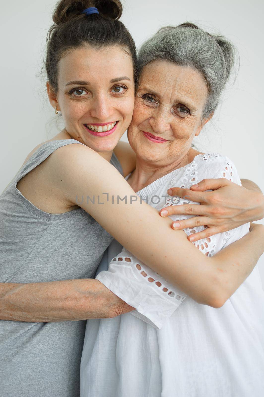 Happy senior mother is hugging her adult daughter, the women are laughing together, sincere family of different age generations having fun on white background, mothers day