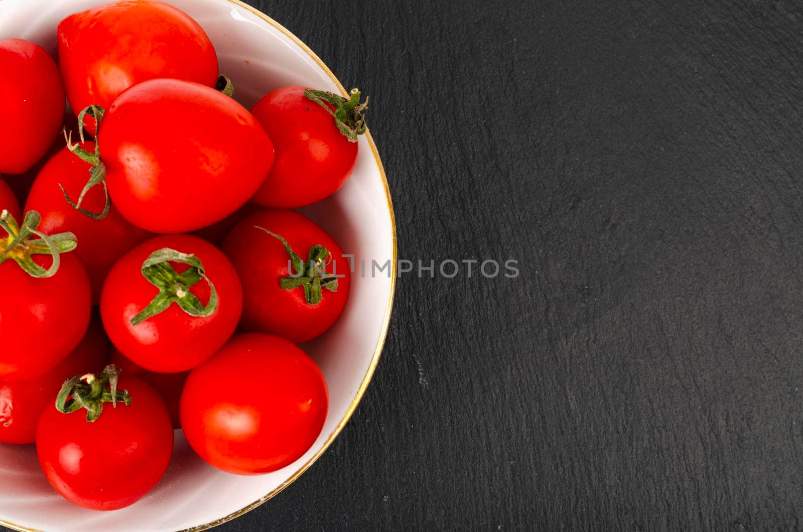 Small red ripe cherry tomatoes in white salad bowl. Studio Photo by ArtCookStudio