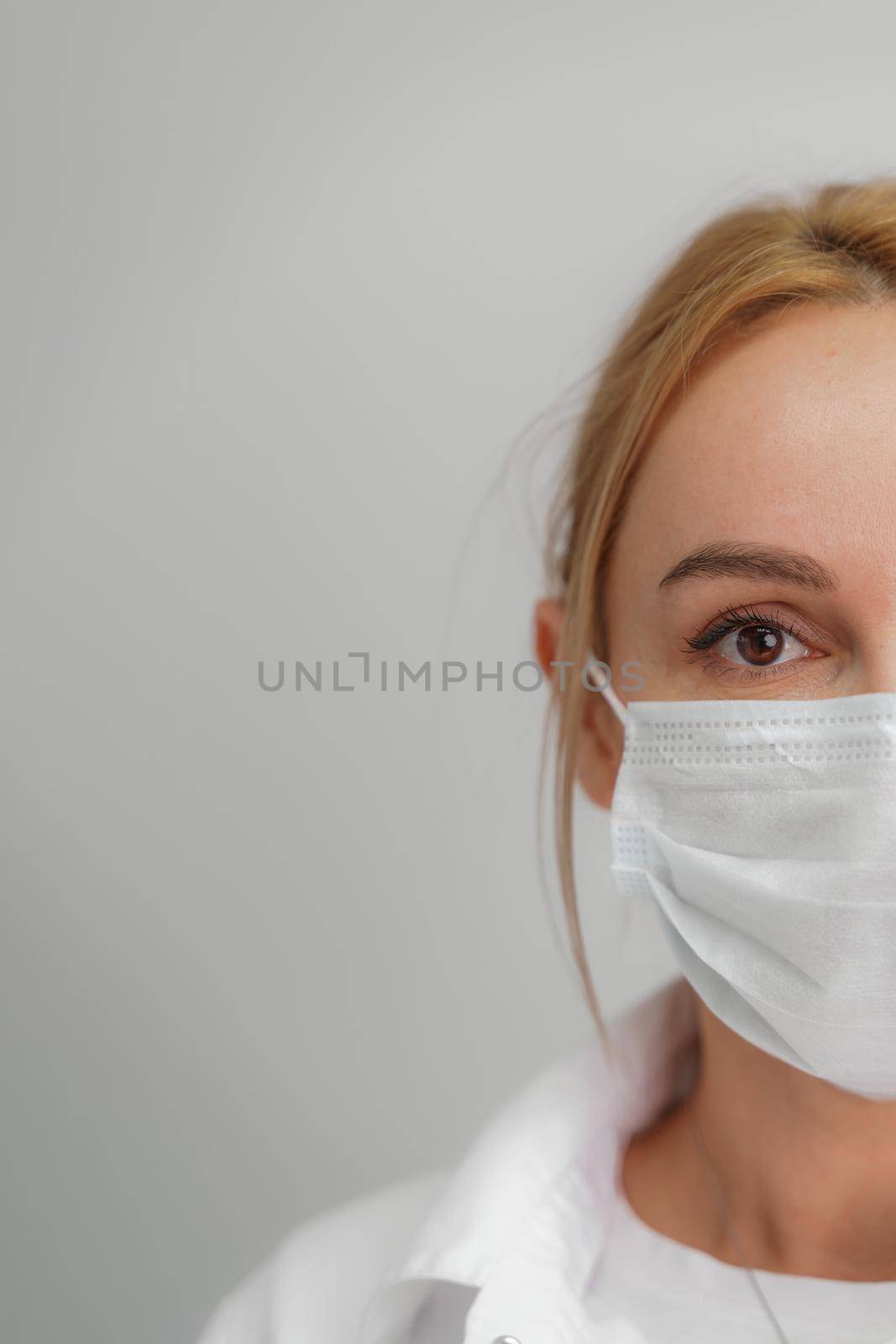 Close-up portrait of a young blonde woman in a medical mask on a light background. Virus protection. Coronovirus covid-19 The concept of a pandemic epidemic. Quarantine. Stay at home. by Matiunina