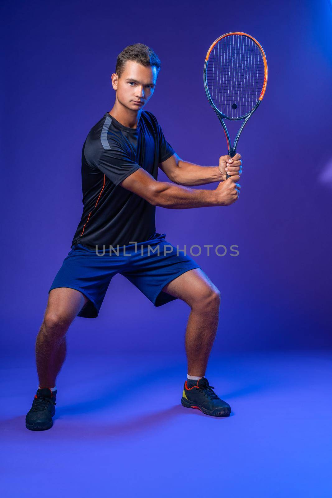 Young tennis player in action against purple background, full length portrait