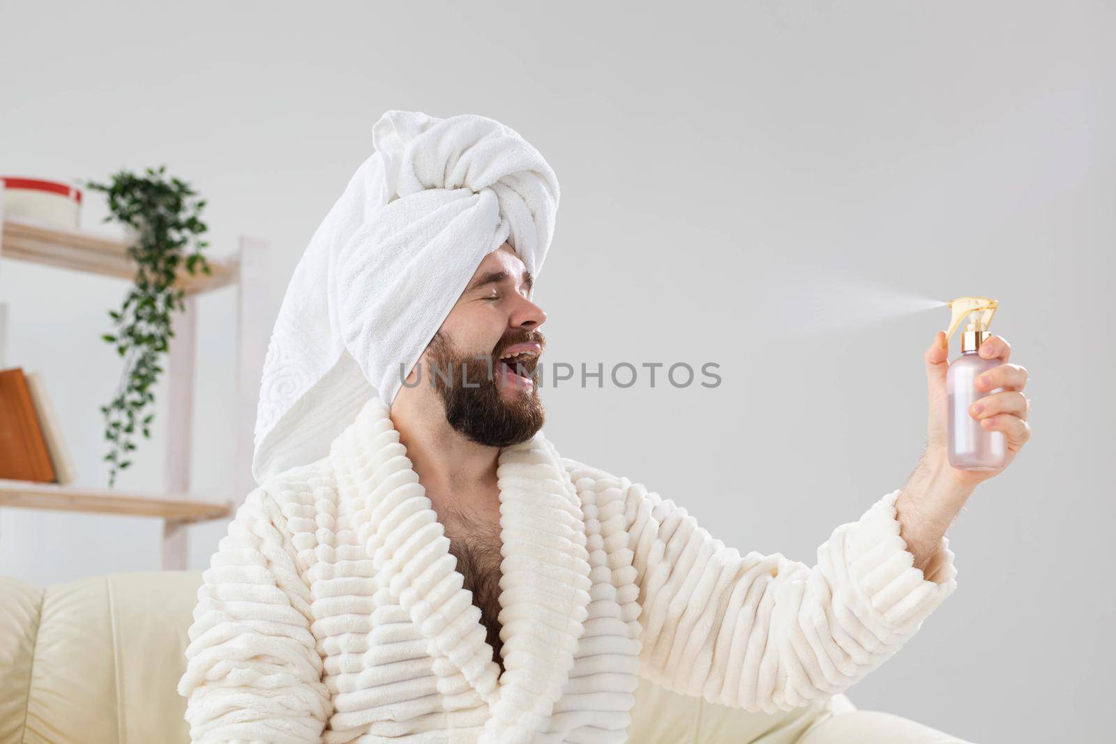 Bearded male with bath towel on his head applying spray water treatment on face. Spa, body and skin care for man concept. by Satura86