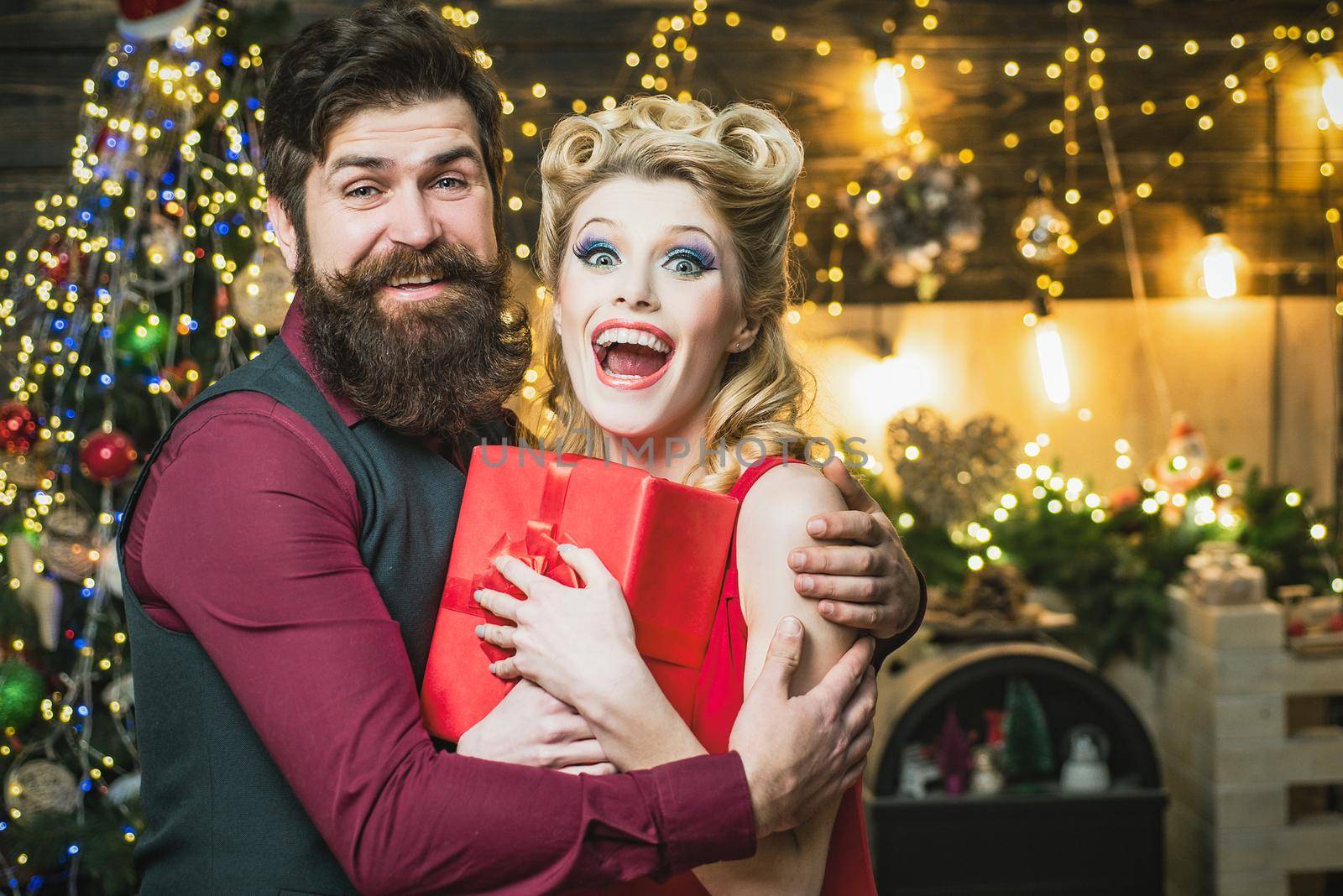 Beautiful Christmas couple with gift hugging. Retro woman with blonde hair and vintage bearded man near the Christmas tree