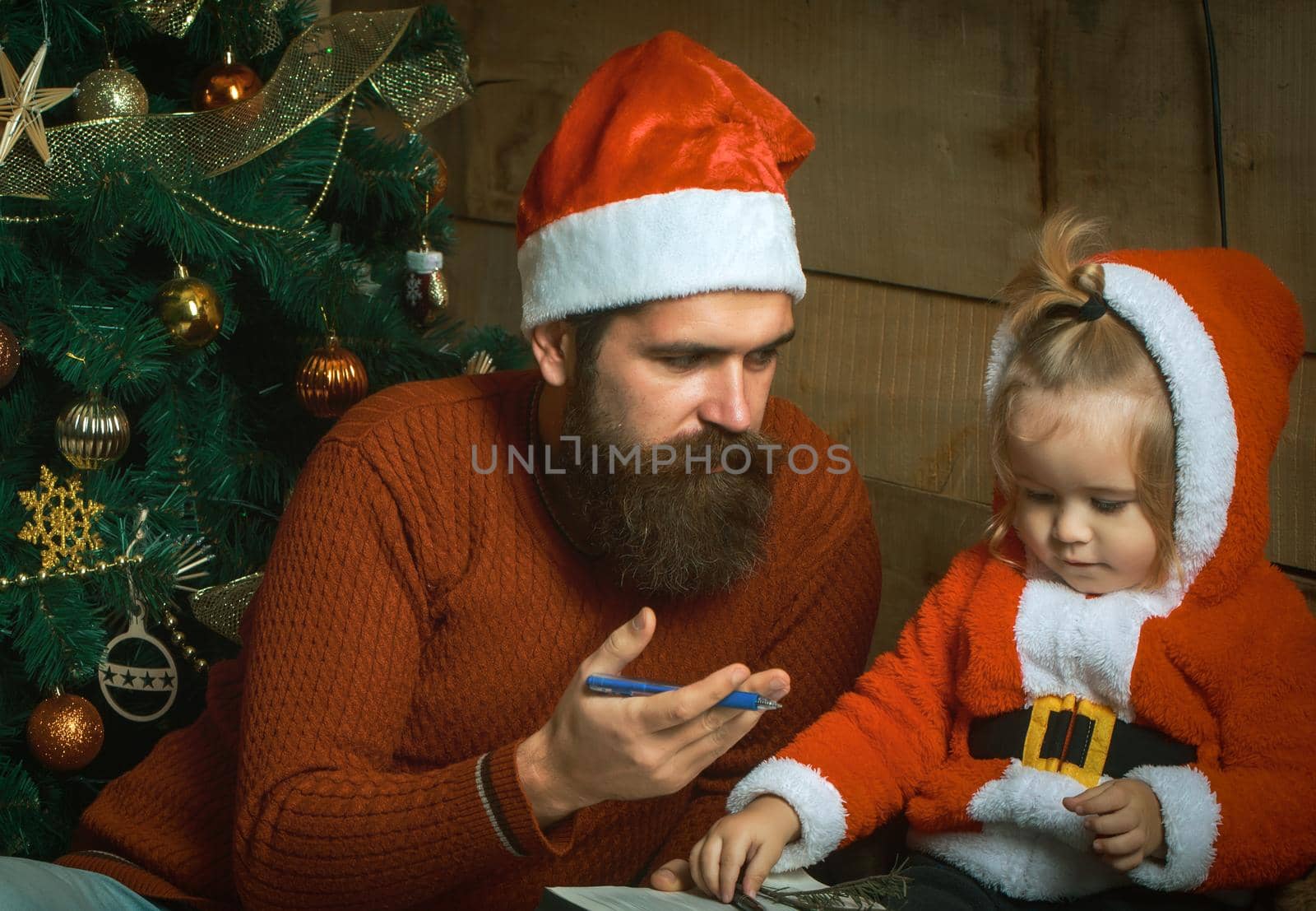 Santa father and baby son at Christmas tree. Winter family holiday and vacation by Tverdokhlib