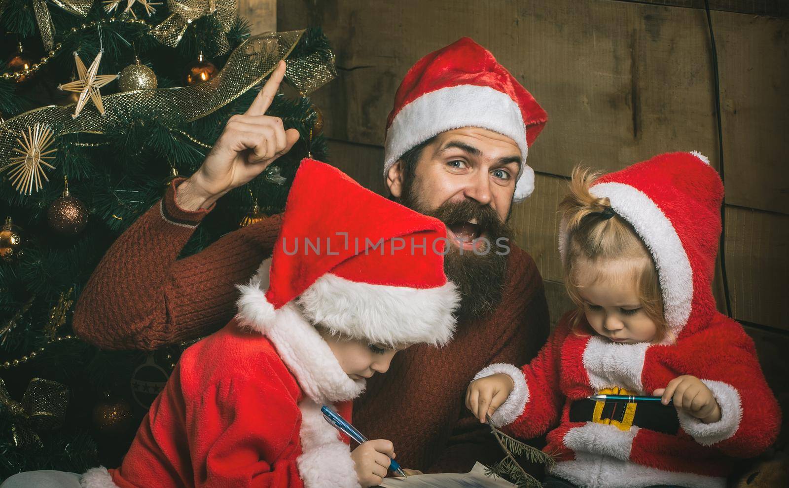 Santa claus with kids at Christmas tree. Xmas celebration, fathers day. Christmas happy children and father read book.