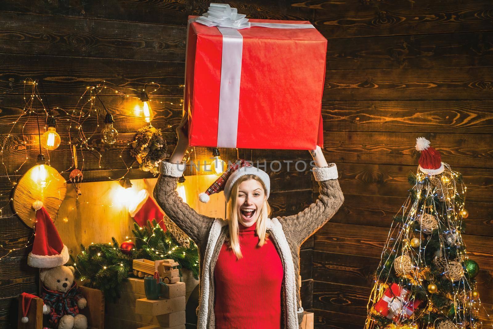 Funny blonde in christmas hat and gifts celebrating christmas holidays hold big box on head