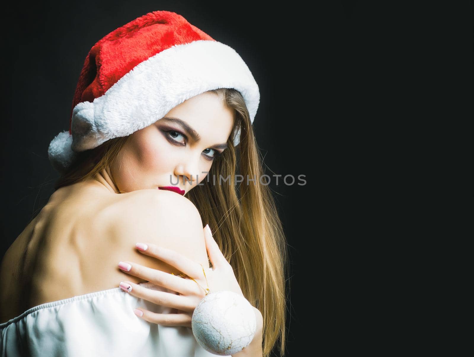 Beautiful young woman in santa hat standing in studio on black background.