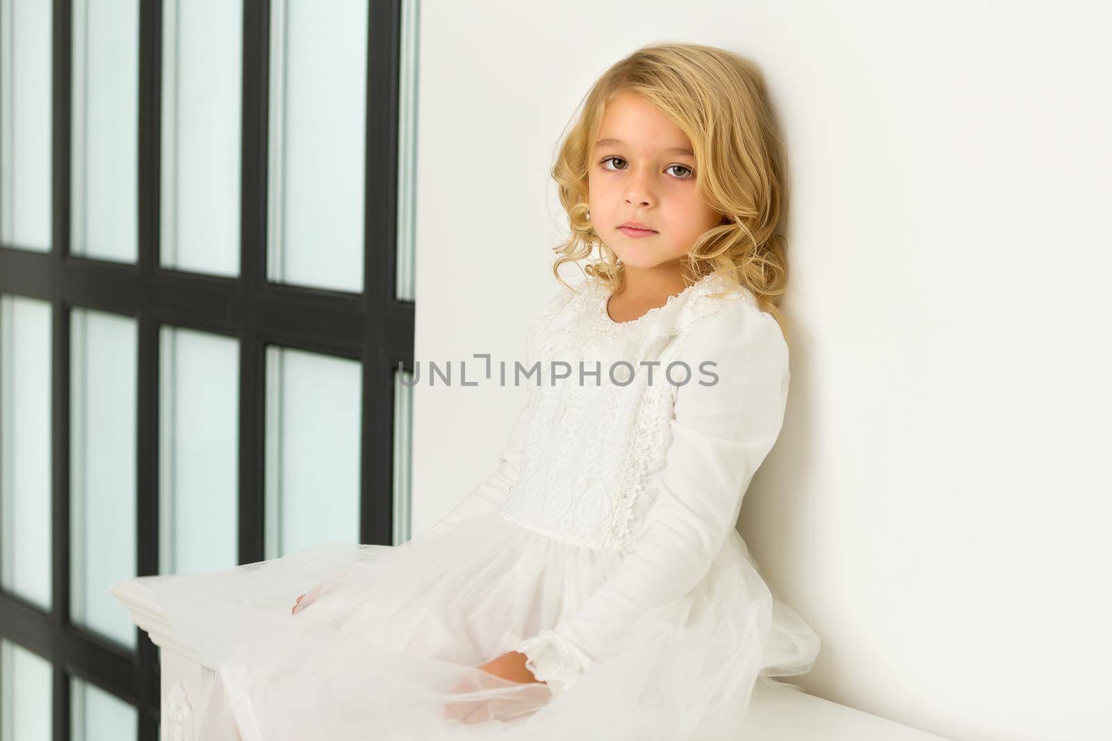Charming little girl near a large panoramic window in a large studio. The concept of childhood, and and fashion.