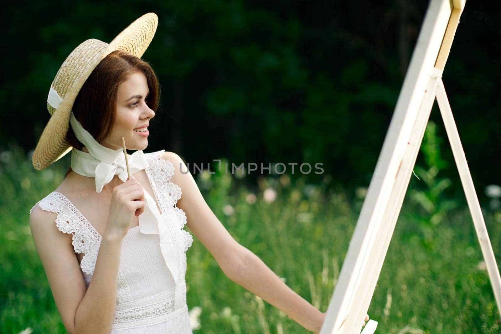 Woman in white dress paints a picture on nature easel. High quality photo