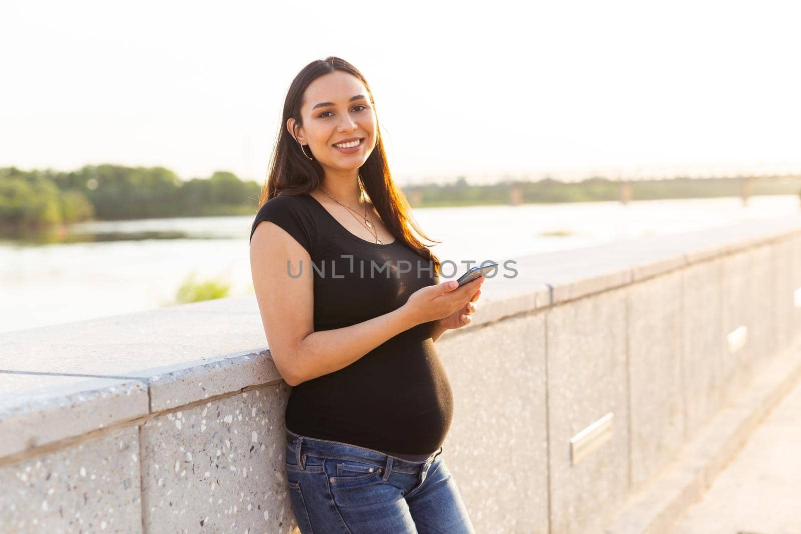 Pregnant woman with smartphone outdoors. Pregnancy, technology and communication.