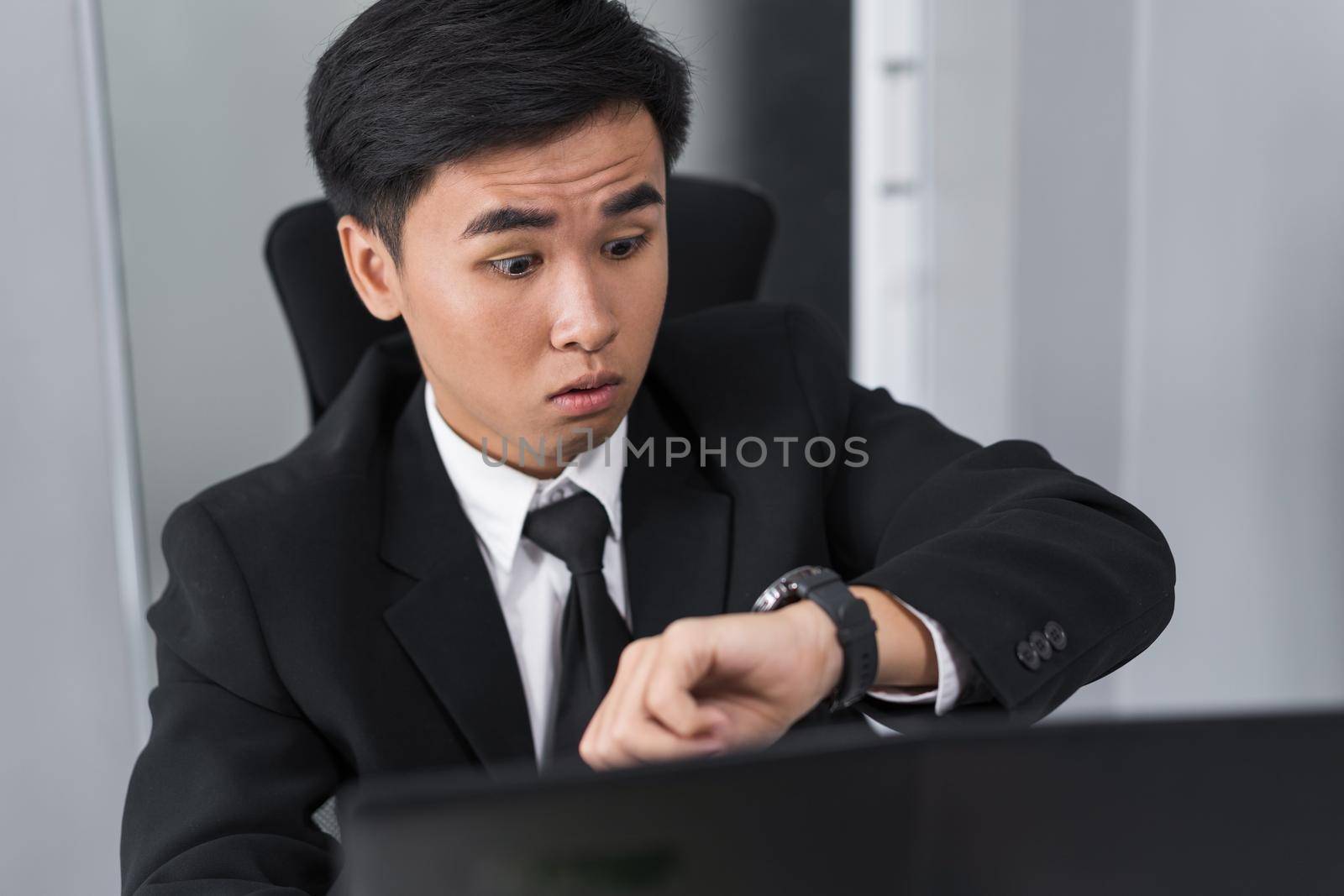 young business man checking time on watch while using laptop