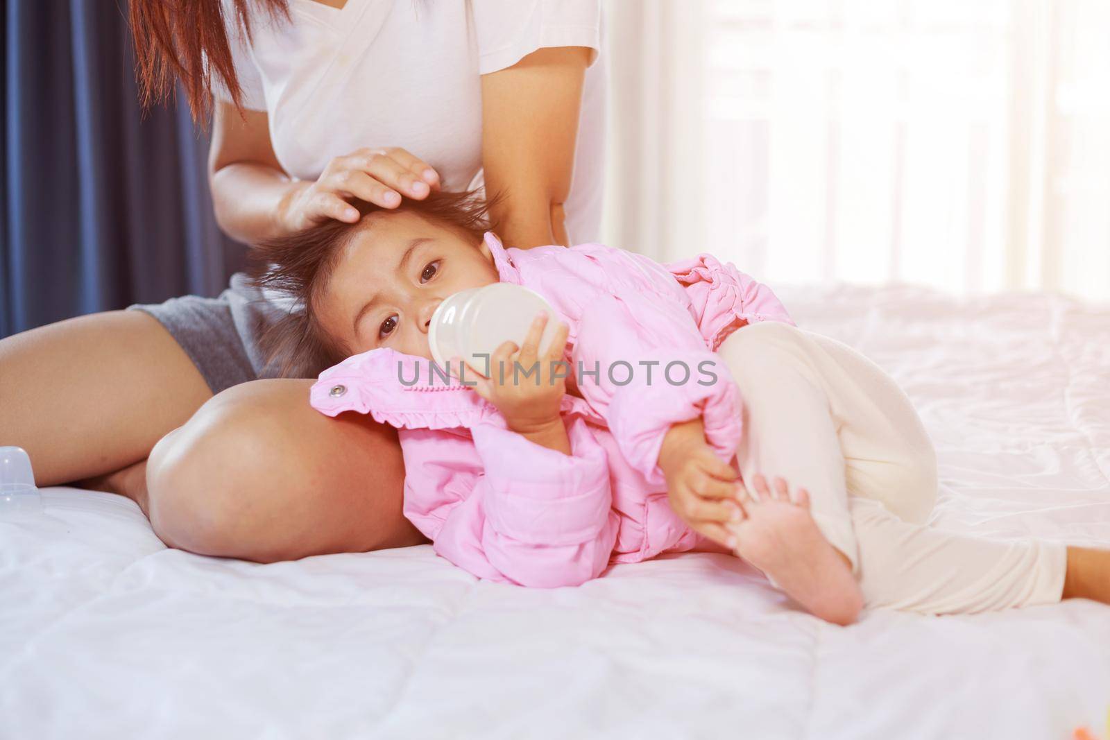 baby drinking a milk from bottle with mother on bed by geargodz