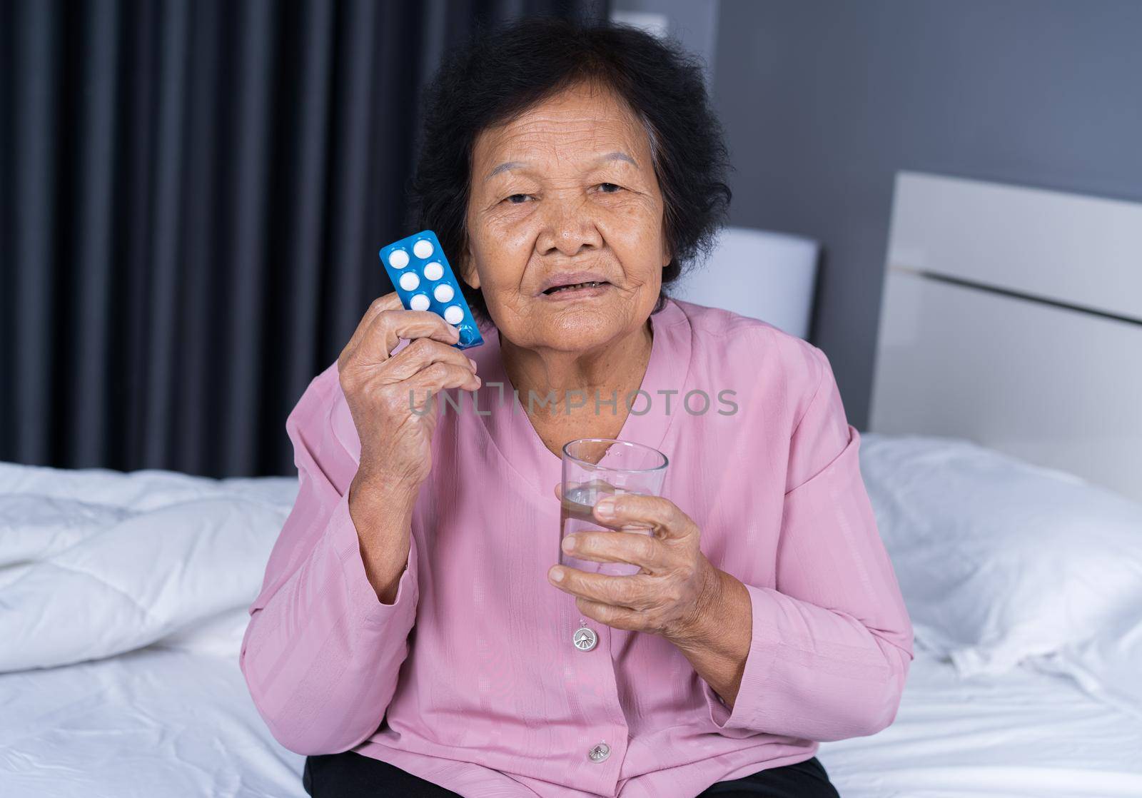 senior woman taking pill with glass of water in bed by geargodz