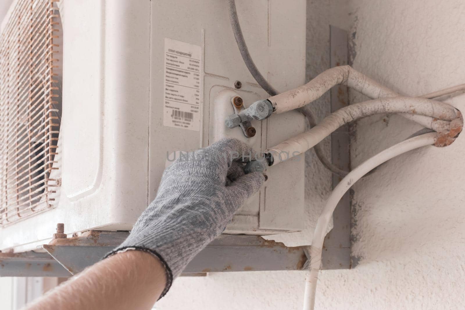 The hand of an air conditioner repair and maintenance specialist in a construction glove working with air-conditioned old equipment.