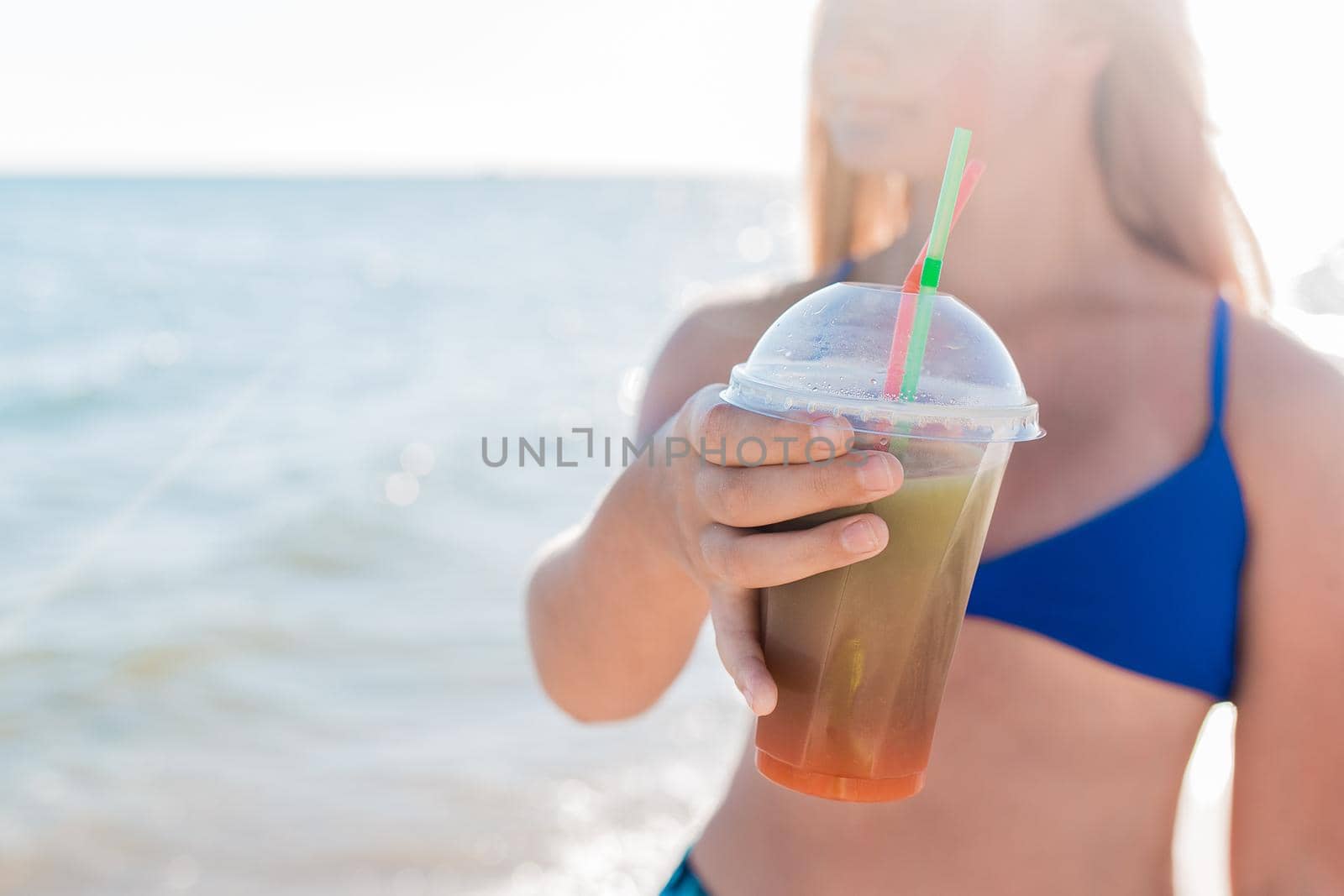 A young girl teenager holds and drink a colored cold non-alcoholic cocktail in her hand against the background of the sea beach.