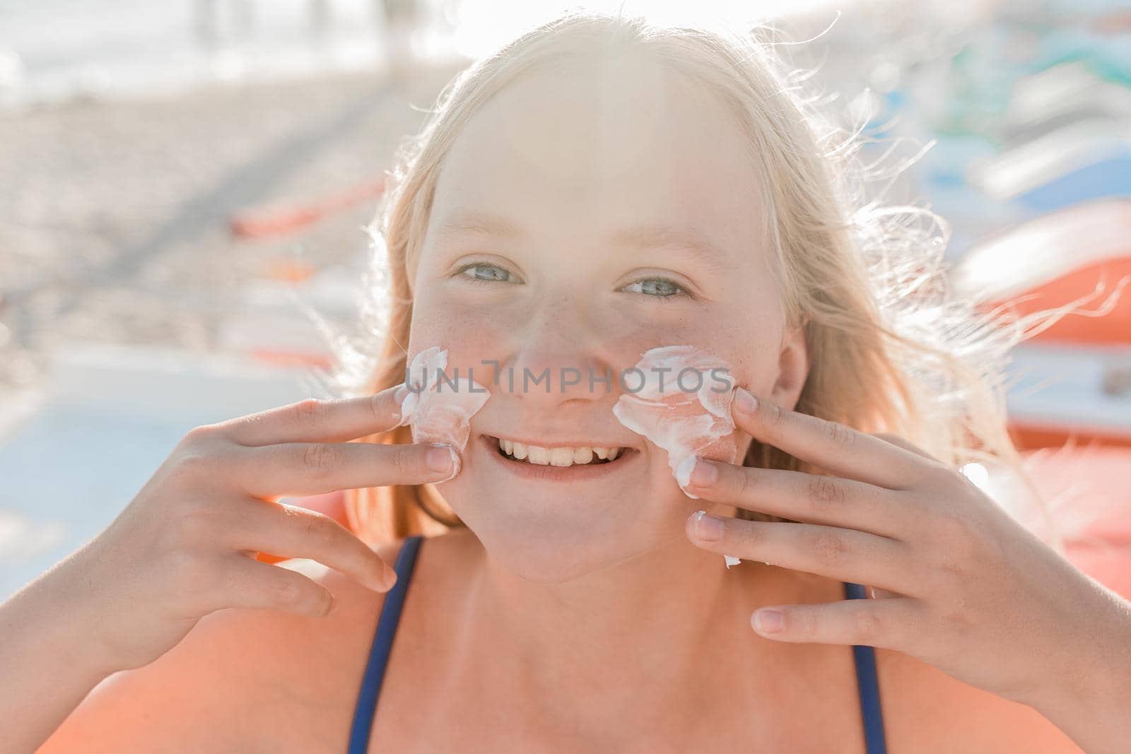 Close-up portrait of a young sweet and happy teenage girl smearing sunscreen on her face.