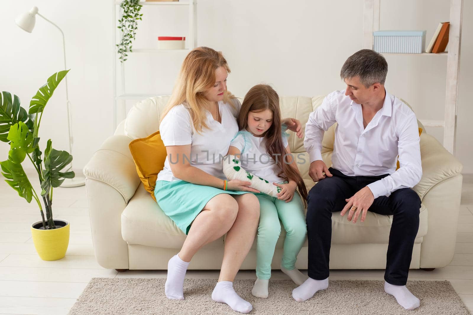 Family sitting on sofa in their living room. Daughter have injury hand but she is happy be together her family. by Satura86