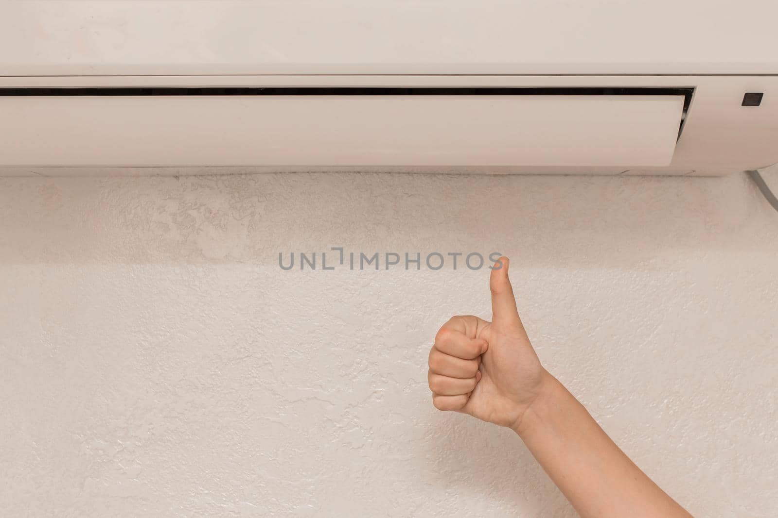 The girl's hand shows the class thumbs up under air conditioner on the wall in the room background.