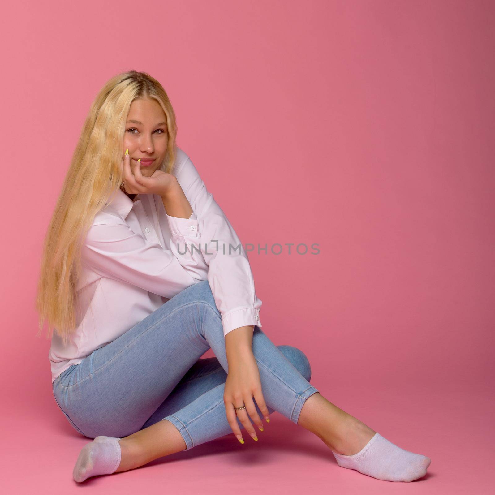 Teen girl teenager sitting on the floor in the studio. The concept of style and fashion. Isolated on pink background.