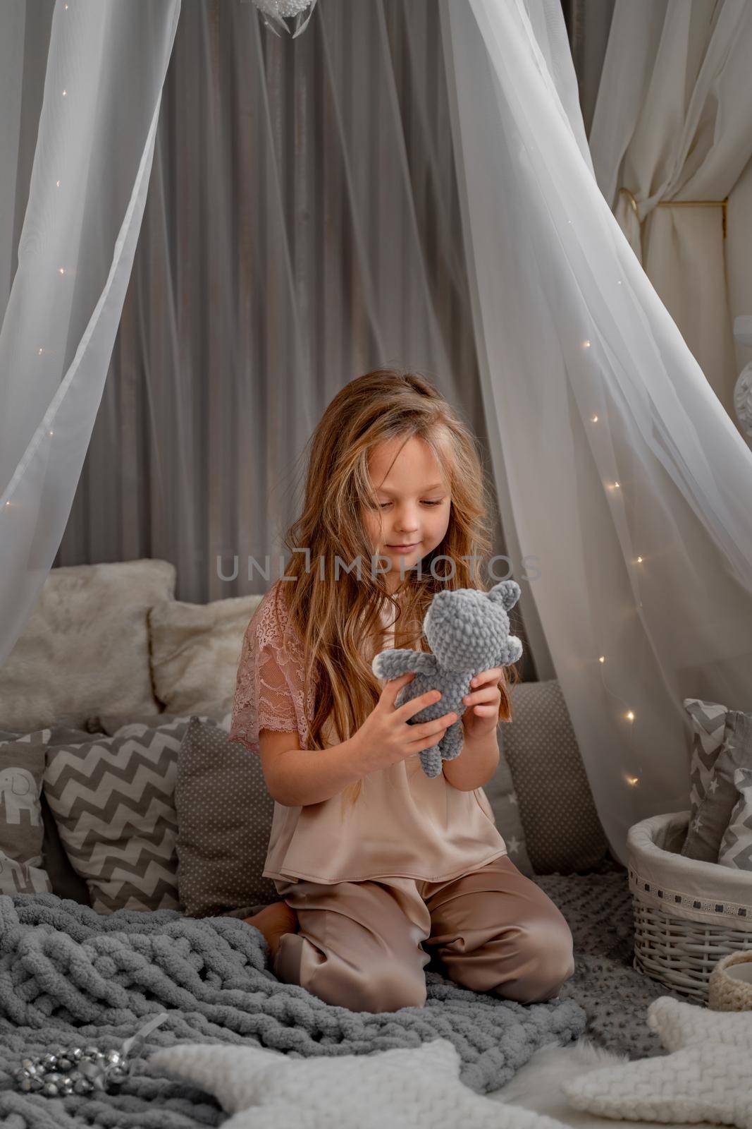 Little cute happy girl in pajamas playing with toys in a white wigwam Close up photo of a happy child. by Matiunina