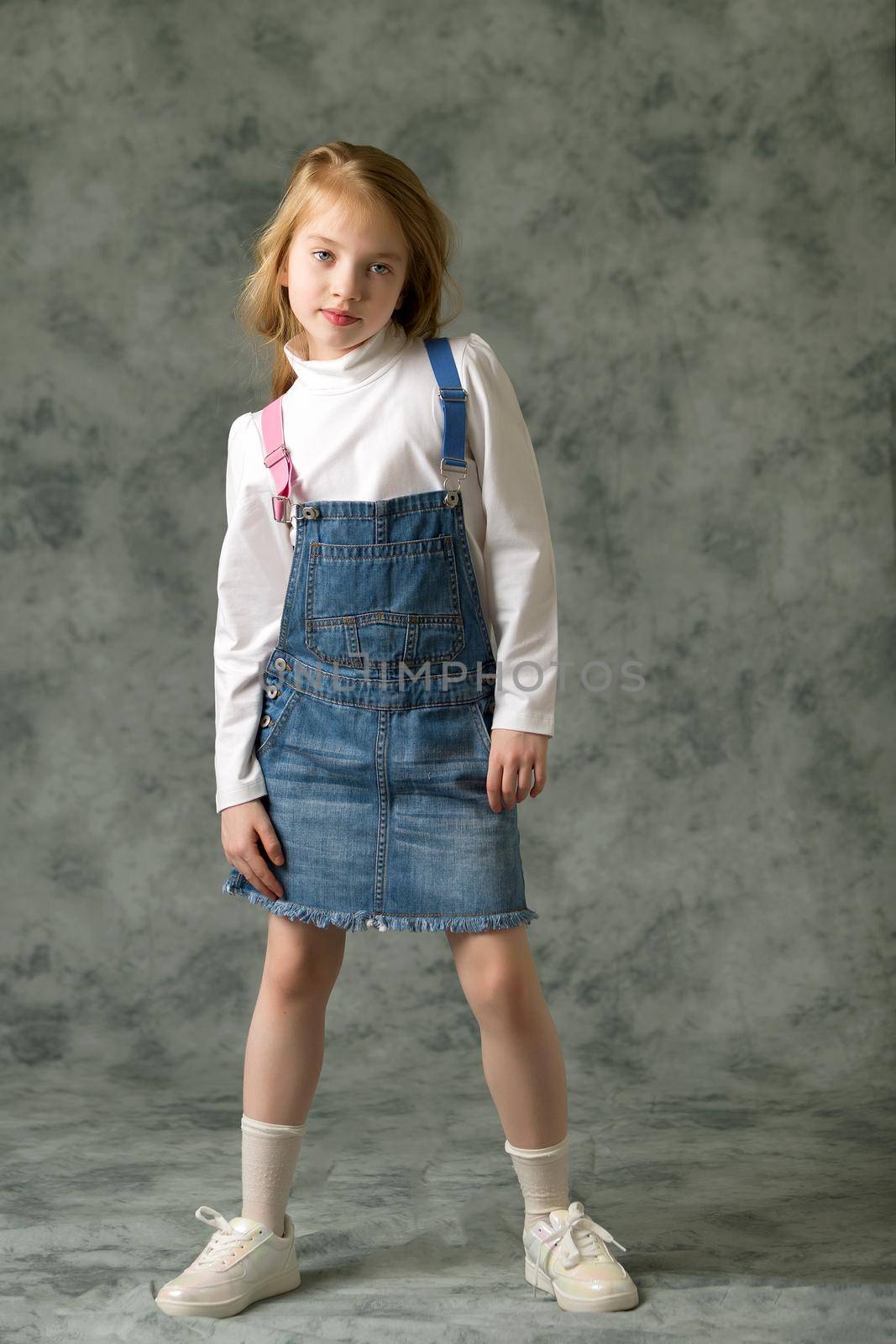 Beautiful little girl in a short denim dress. Concept of beauty and fashion, happy childhood.