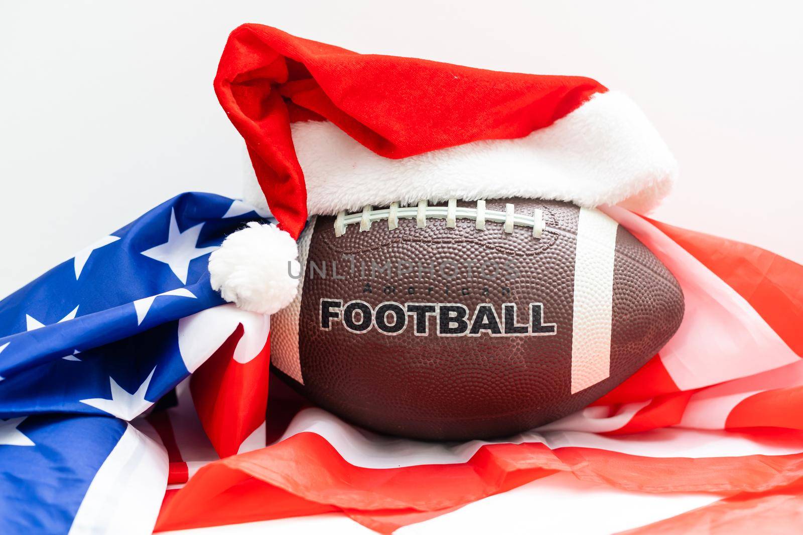 A souvenir ball for rugby or american football in a red santa claus hat on a green background. Preparation for design of tickets, posters, postcards or business cards on the subject of the sports
