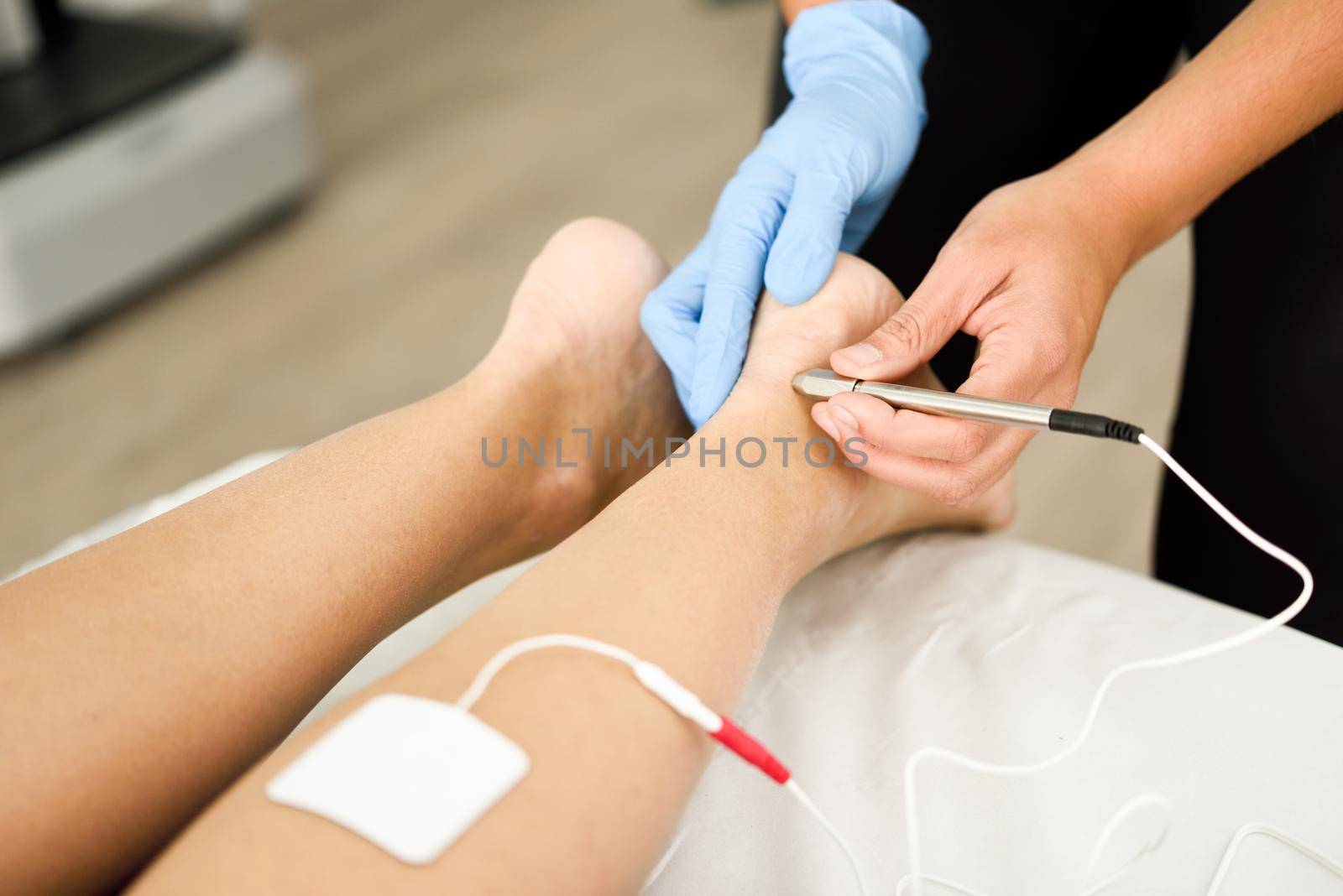 Electroacupuncture dry with needle connecting machine used by acupunturist on female patient for acupuncture guided by EPI Intratissue Percutaneous Electrolisis. Electro stimulation in physical therapy to ankle of a young woman in physiotherapy center.