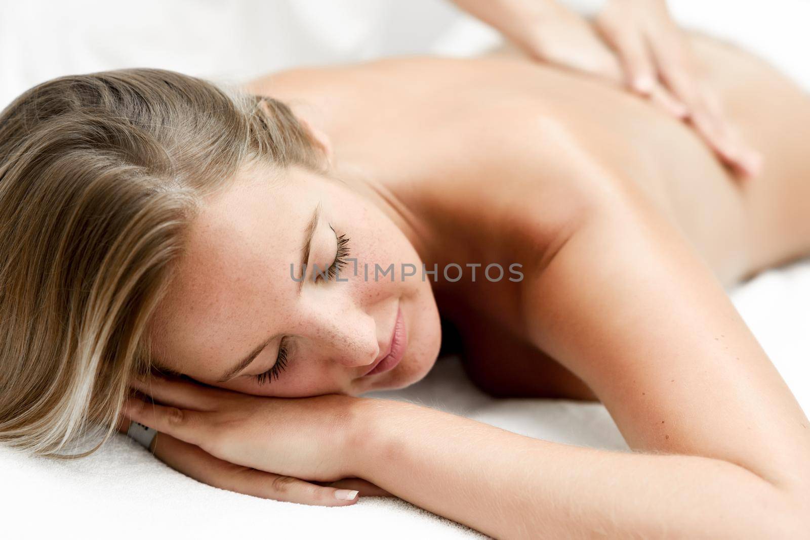 Young blond woman having massage in the spa salon. Massage and body care. Body massage treatment.