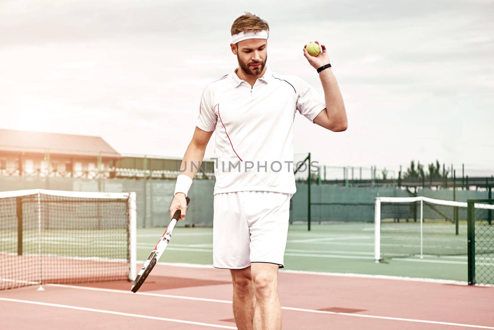 Work hard, play hard. Handsome man standing on the tennis court with the racket and the ball in his hands by friendsstock