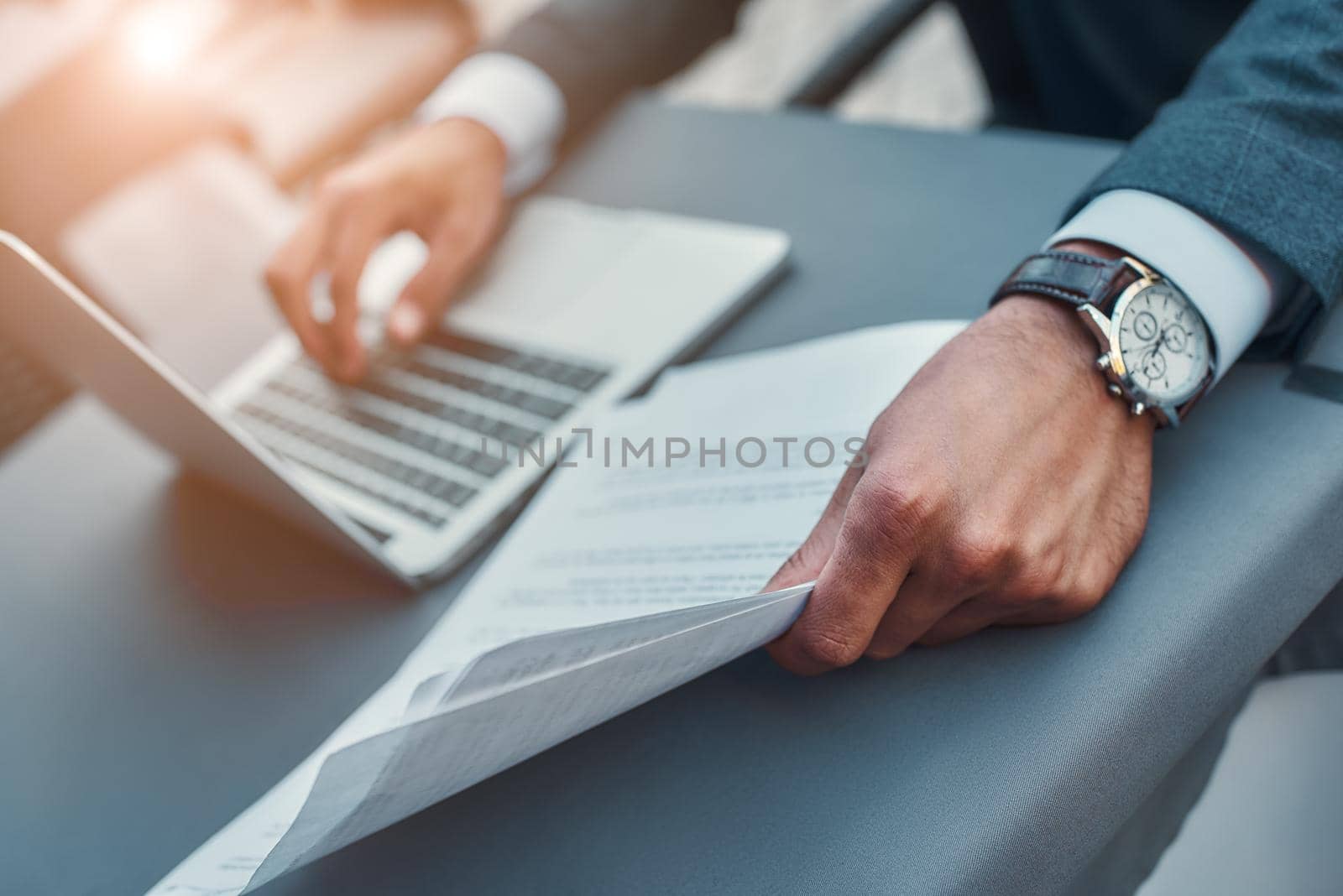 Cropped photo of businessman with watch on his hand working with laptop and documents while sitting in restaurant outdoors by friendsstock