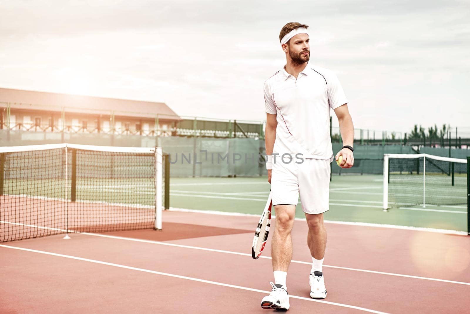 Tennis player in white sportswear with the racket and the ball in his hands is going to play tennis. Horizontal shot