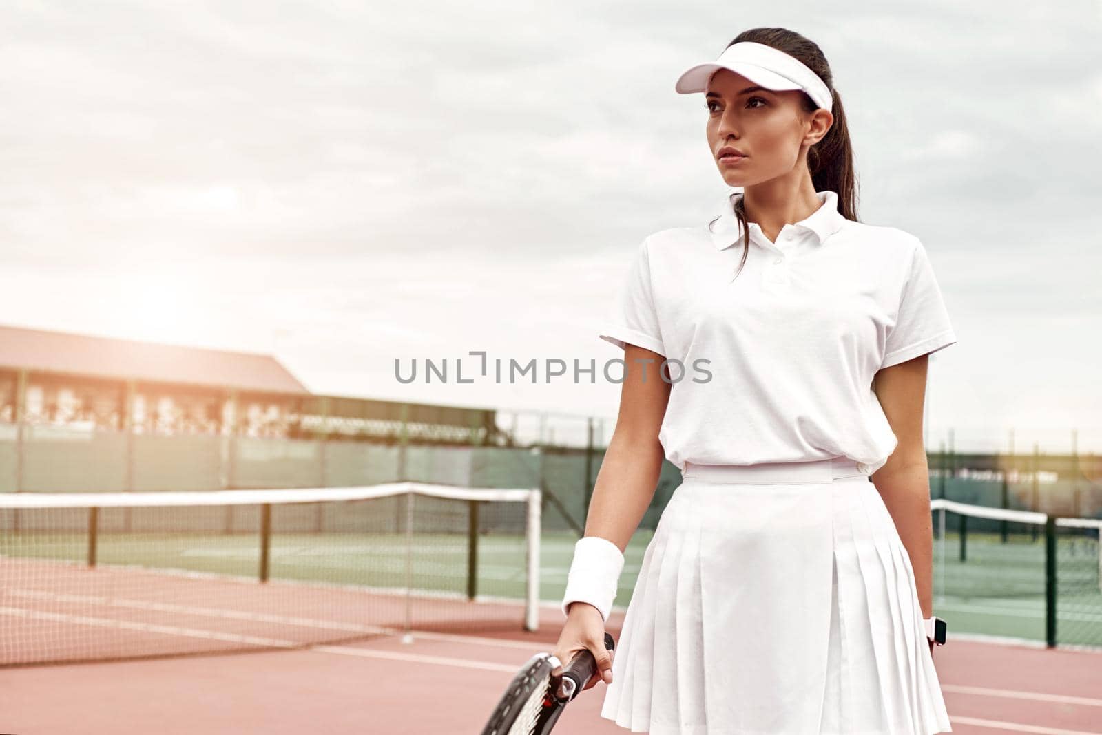 Attractive sportswoman in white sportswear with a racket in her hand standing on the court