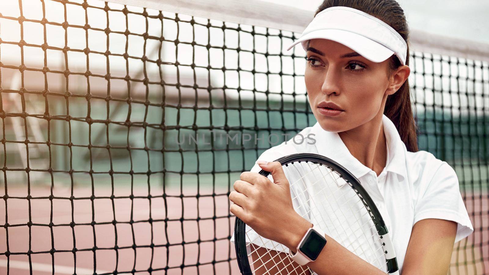 Portrait of female tennis player sitting with a racket on a court, looking away. Healthy lifestyle. Horizontal shot