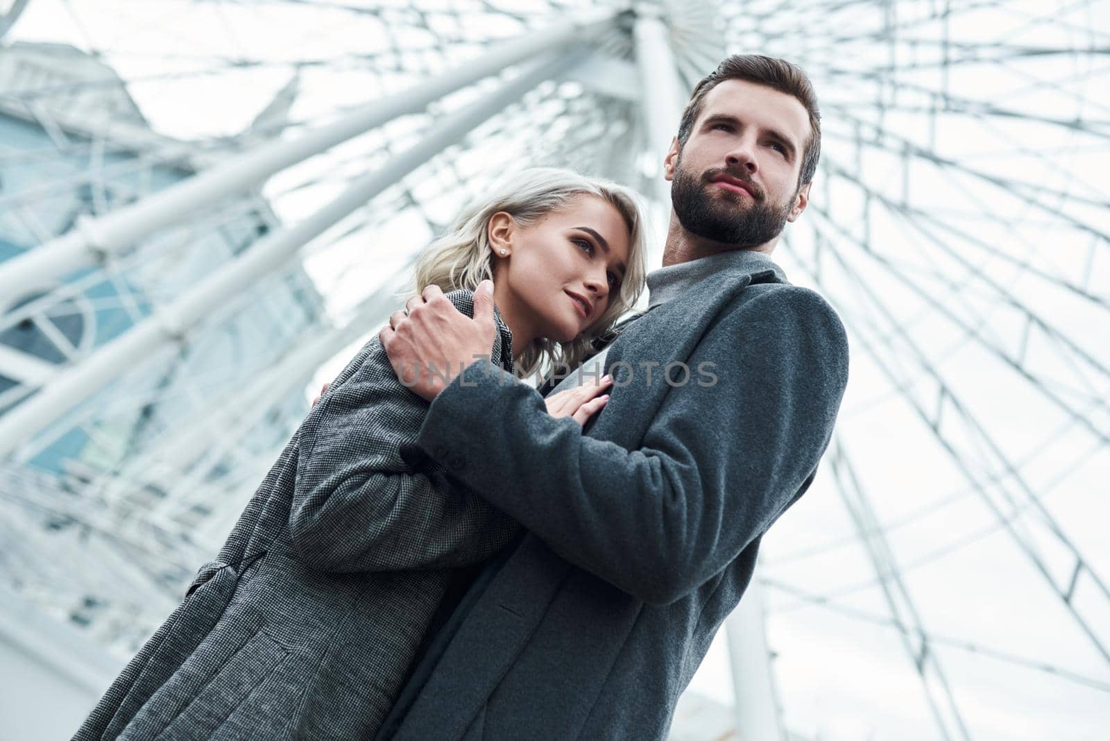 Romantic date outdoors. Young couple standing at entertainment park hugging looking aside pensive bottom view close-up