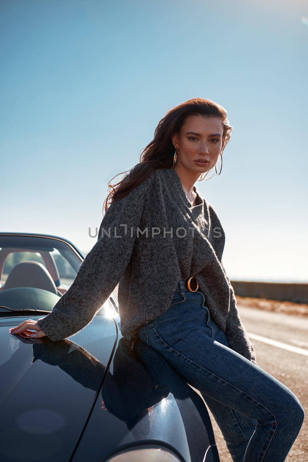 Young woman near roofless car outdoors on sunny day near the empty road. No people, sportive black car