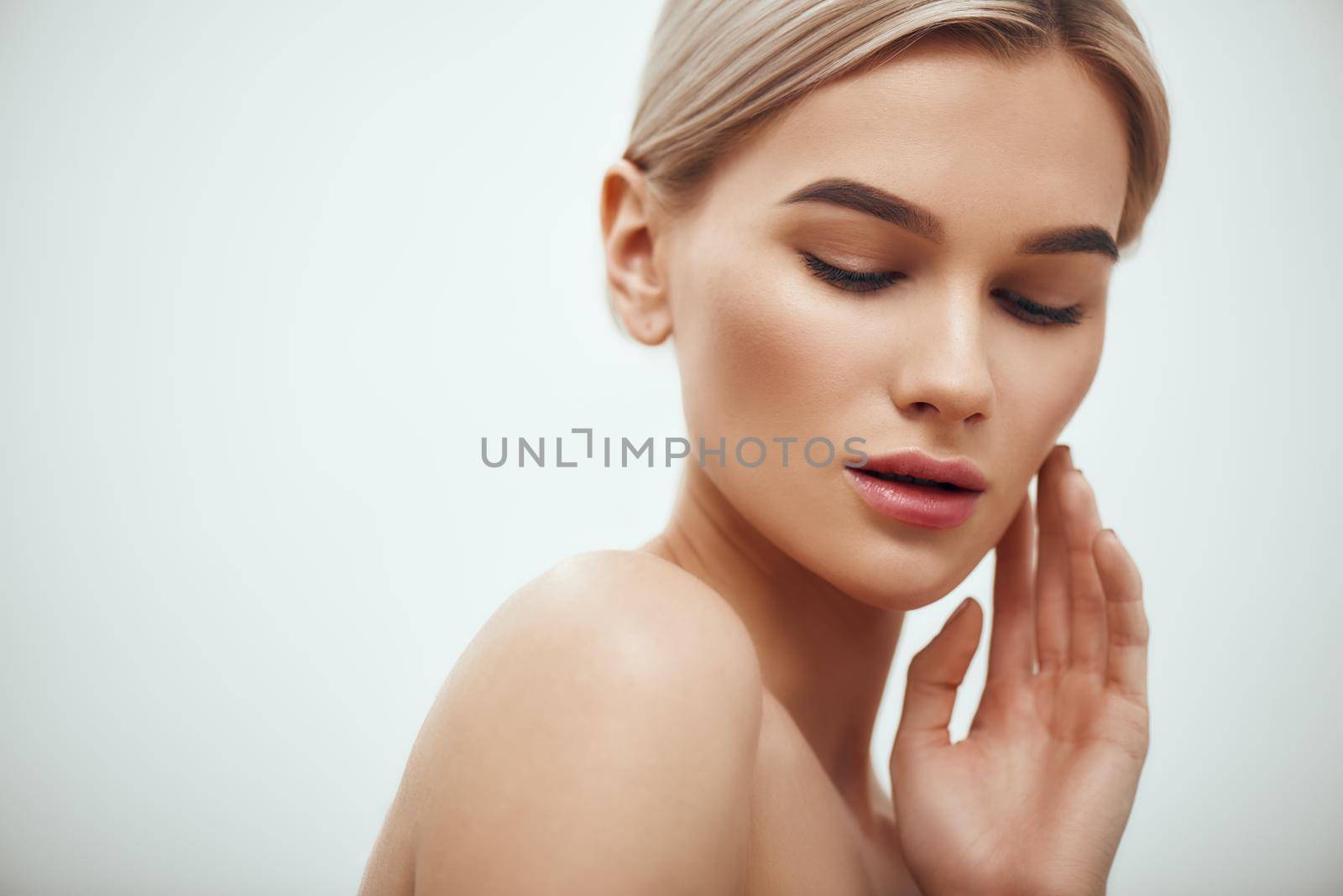 I love my skin. Attractive young blonde woman keeping eyes closed and touching her face while standing against grey background. Skin care. Beauty concept