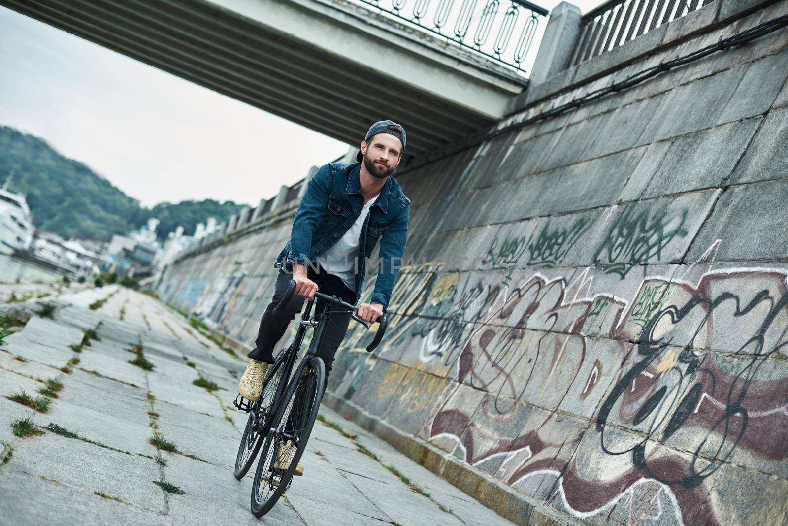 Outdoors leisure. Young stylish man riding bicycle on city street looking forward smiling happy by friendsstock