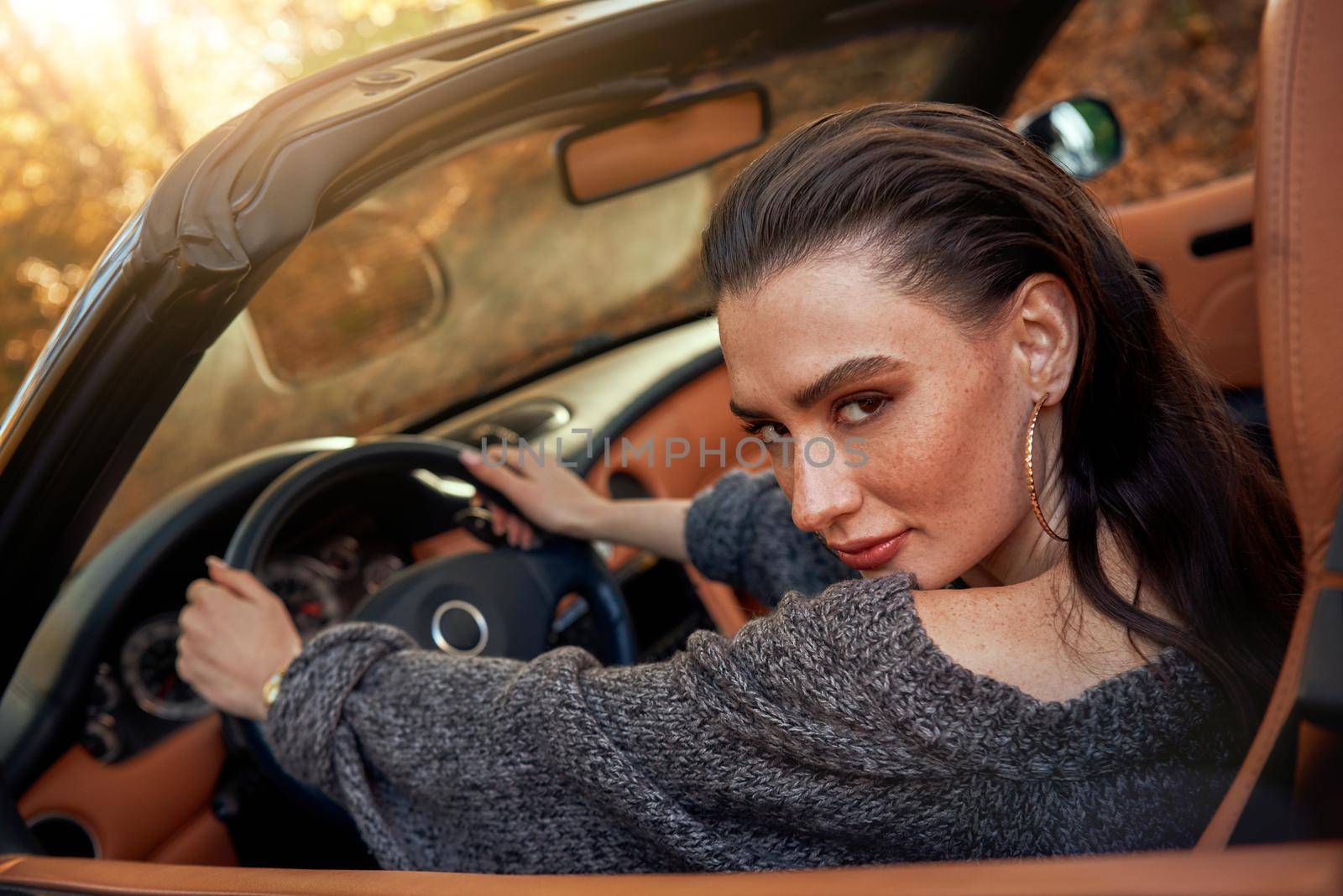 Sexy young woman in jeans and in a grey sweater sits in a cabriolet by friendsstock