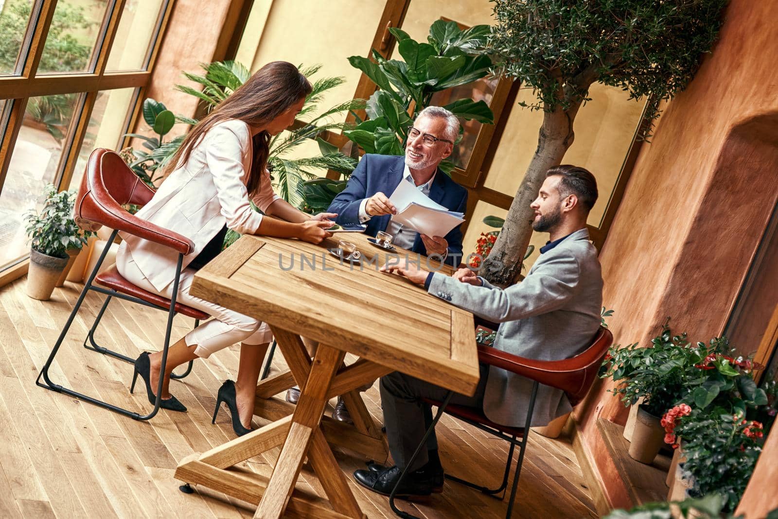 Business lunch. Three people in the restaurant sitting at table drinking hot coffee discussing project joyful. Team work concept by friendsstock