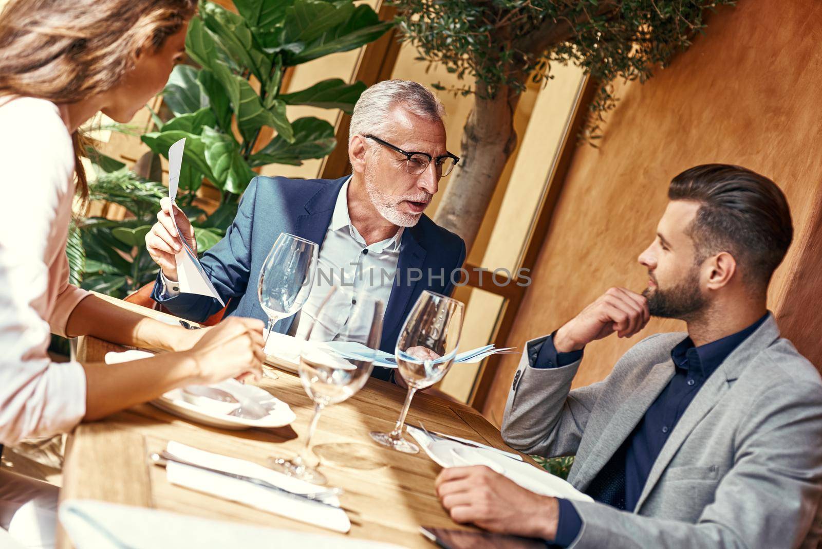 Business lunch. Three people in the restaurant sitting at table negotiating about contract. Team work concept by friendsstock