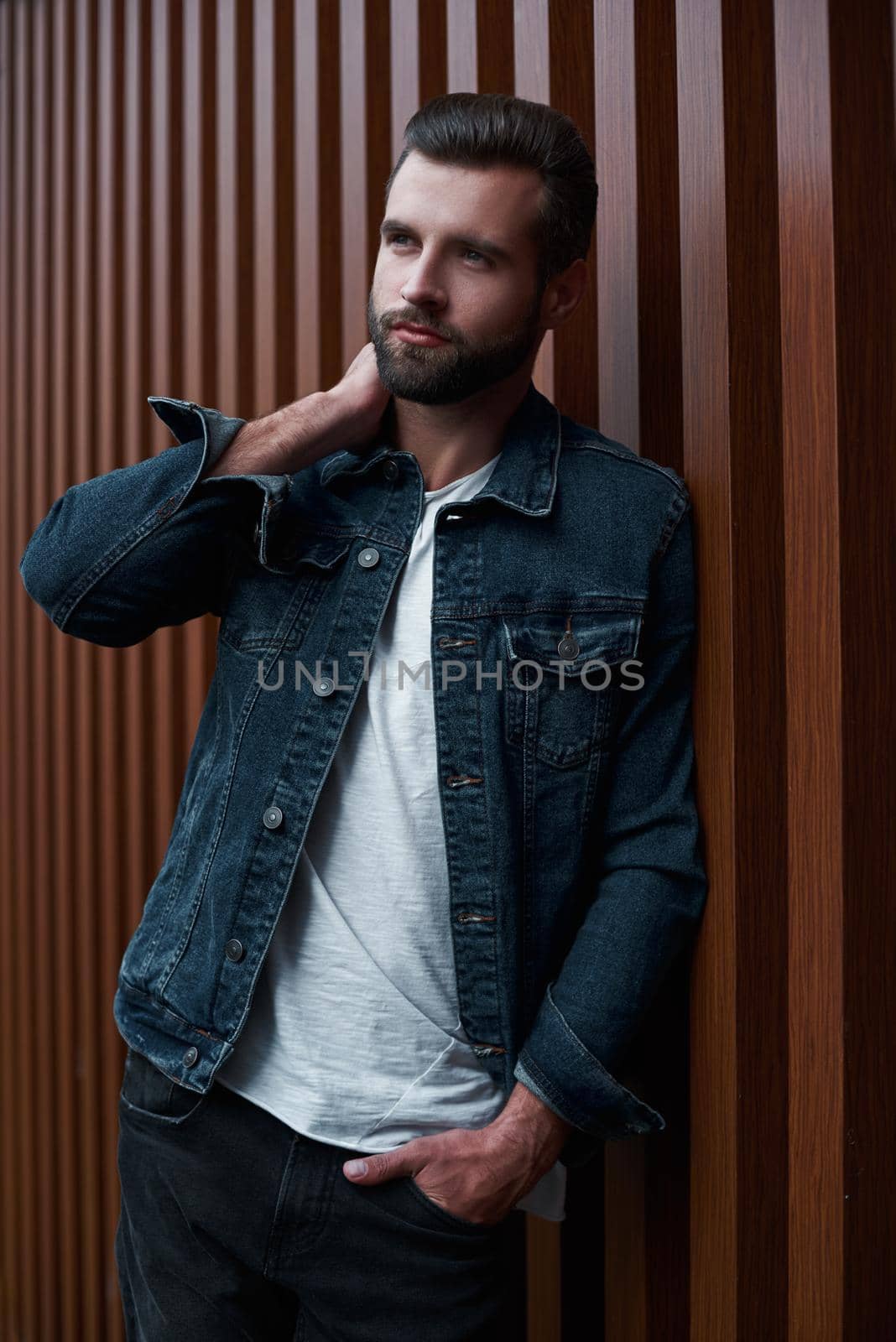 Freestyle. Young man standing leaning on wooden wall isolated touching neck looking aside pensive by friendsstock