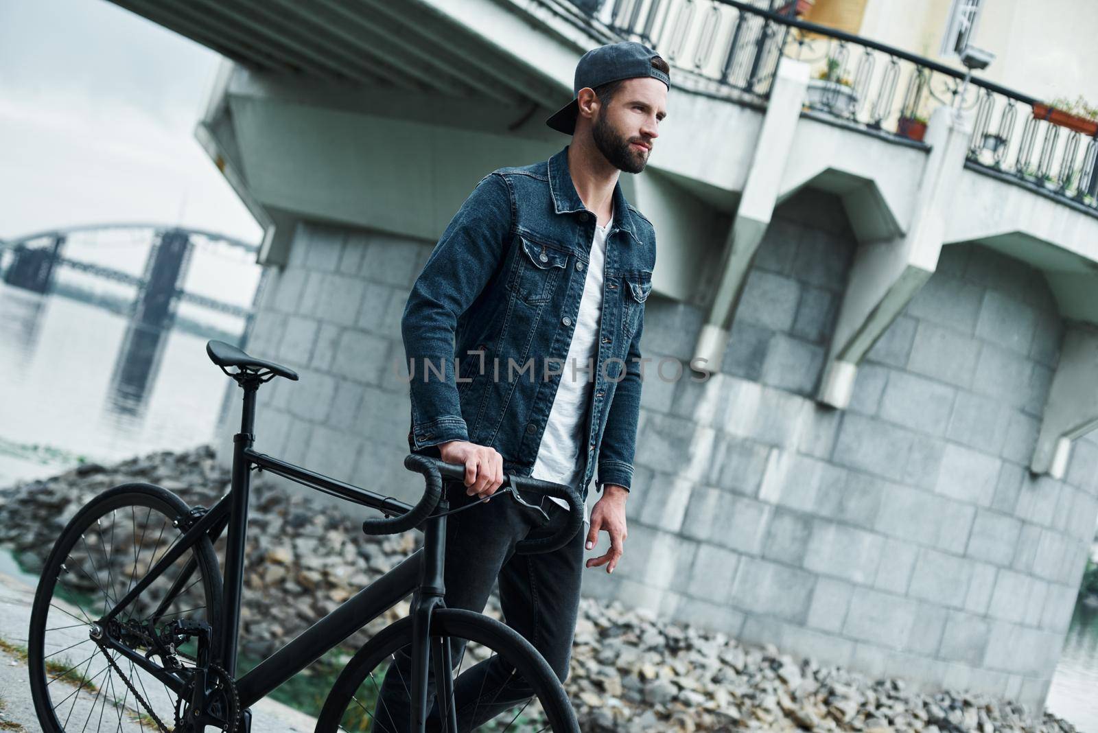 Outdoors leisure. Young stylish man walking on city street with bicycle looking forward confident